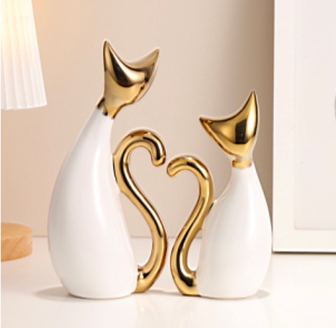 Two white and gold decorative cat figurines with heart-shaped tails on a tabletop