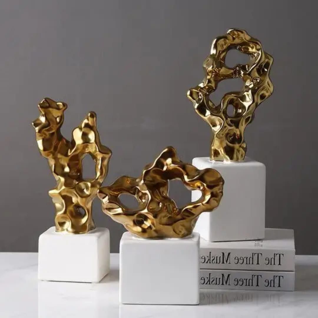 Gold abstract sculpture on a white pedestal beside books and white flowers on a shelf