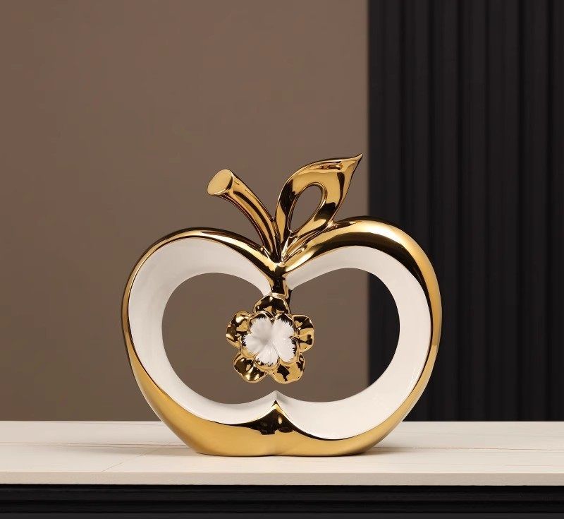 Gold and white apple-shaped ornament with a flower detail on a dark shelf