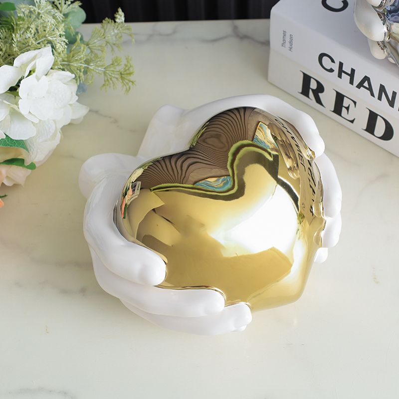 Gold heart-shaped decorative object on a marble surface, framed by white floral accents and books.