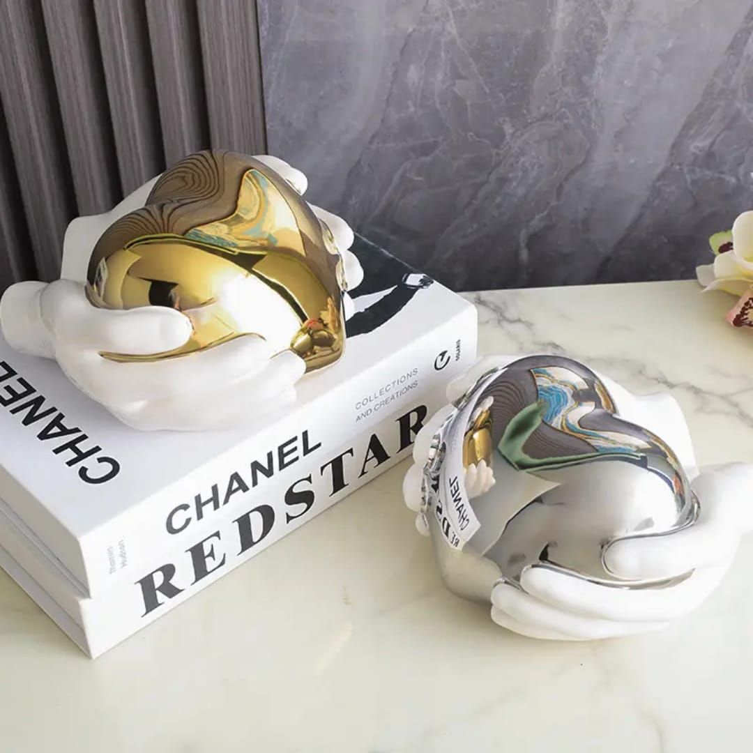 Gold heart-shaped decorative object on a marble surface, framed by white floral accents and books.