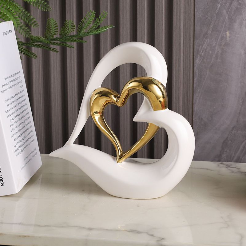 White and gold heart sculpture on a marble surface beside a book, against a gray backdrop