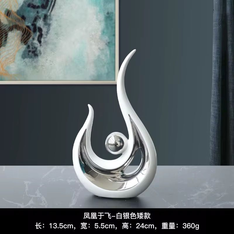 Abstract gold-and-white flame-shaped tabletop sculpture with a central sphere on a gray surface.