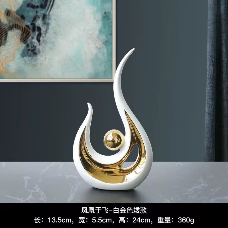 Abstract gold-and-white flame-shaped tabletop sculpture with a central sphere on a gray surface.