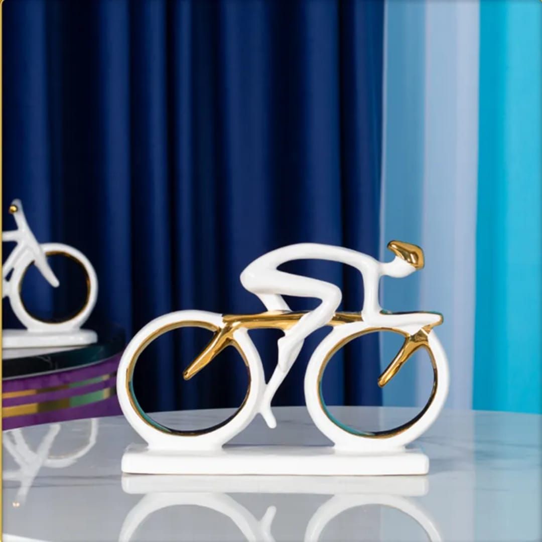 White and gold bicycle sculpture on a white base against blue curtains, with a blurred bike in the background
