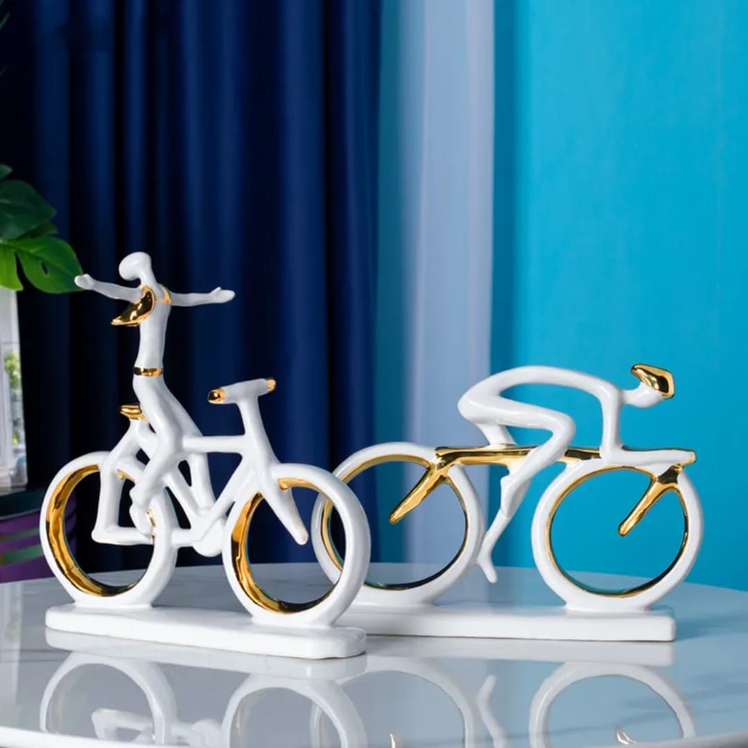White and gold bicycle sculpture on a white base against blue curtains, with a blurred bike in the background