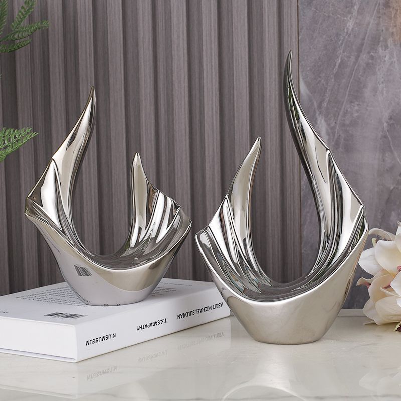 Two silver abstract sculptures on a white tabletop beside stacked books and flowers