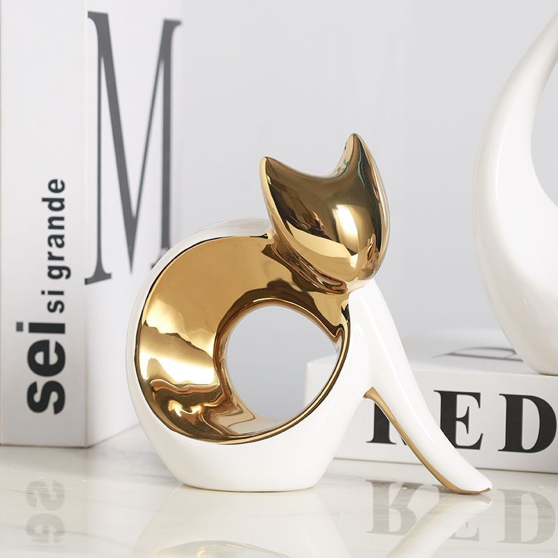 Gold-and-white cat figurine beside white books on a glossy surface