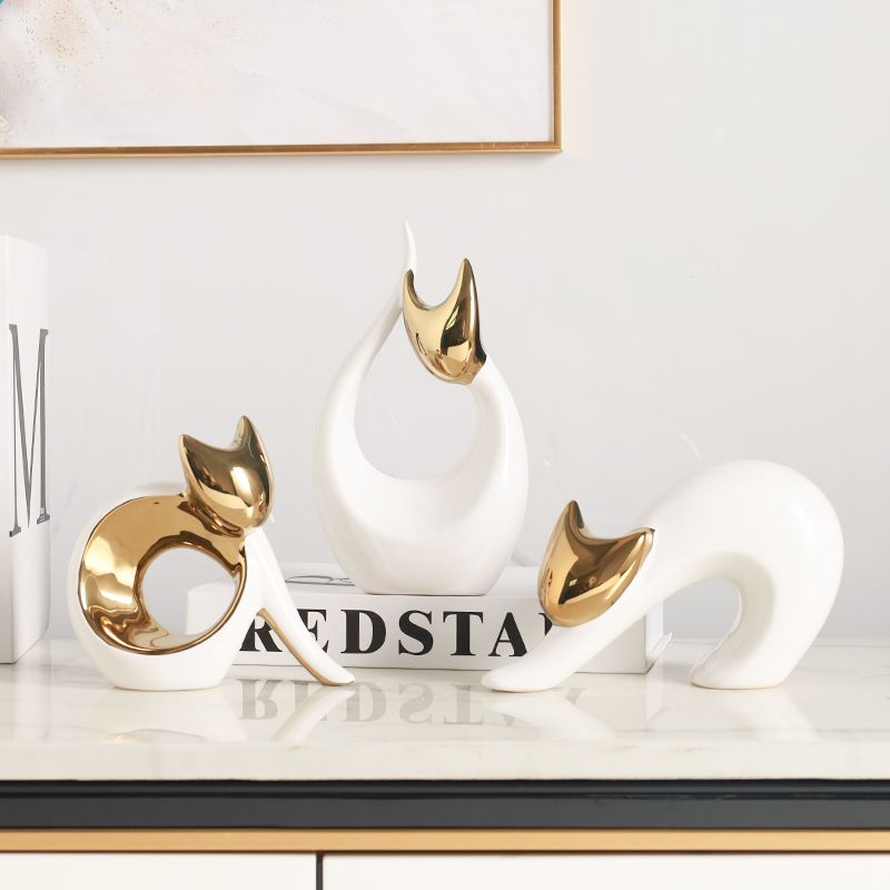 Gold-and-white cat figurine beside white books on a glossy surface