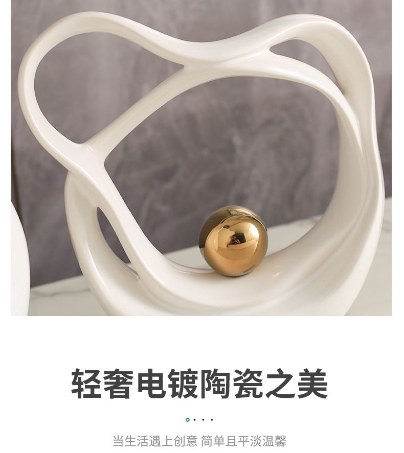 White abstract sculpture holding a gold sphere on a marble surface against a dark backdrop