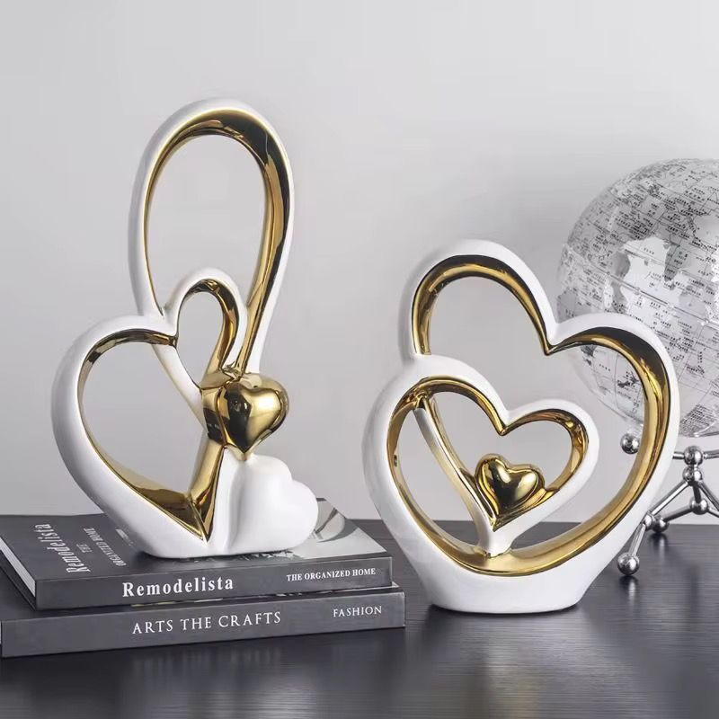 Two gold-and-white heart sculptures on stacked books, with a small white heart ornament and a silver globe.