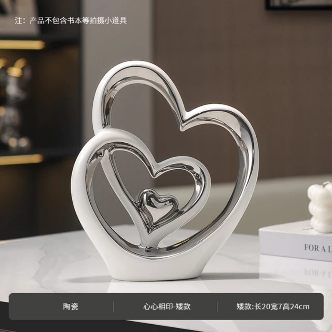 Two gold-and-white heart sculptures on stacked books, with a small white heart ornament and a silver globe.