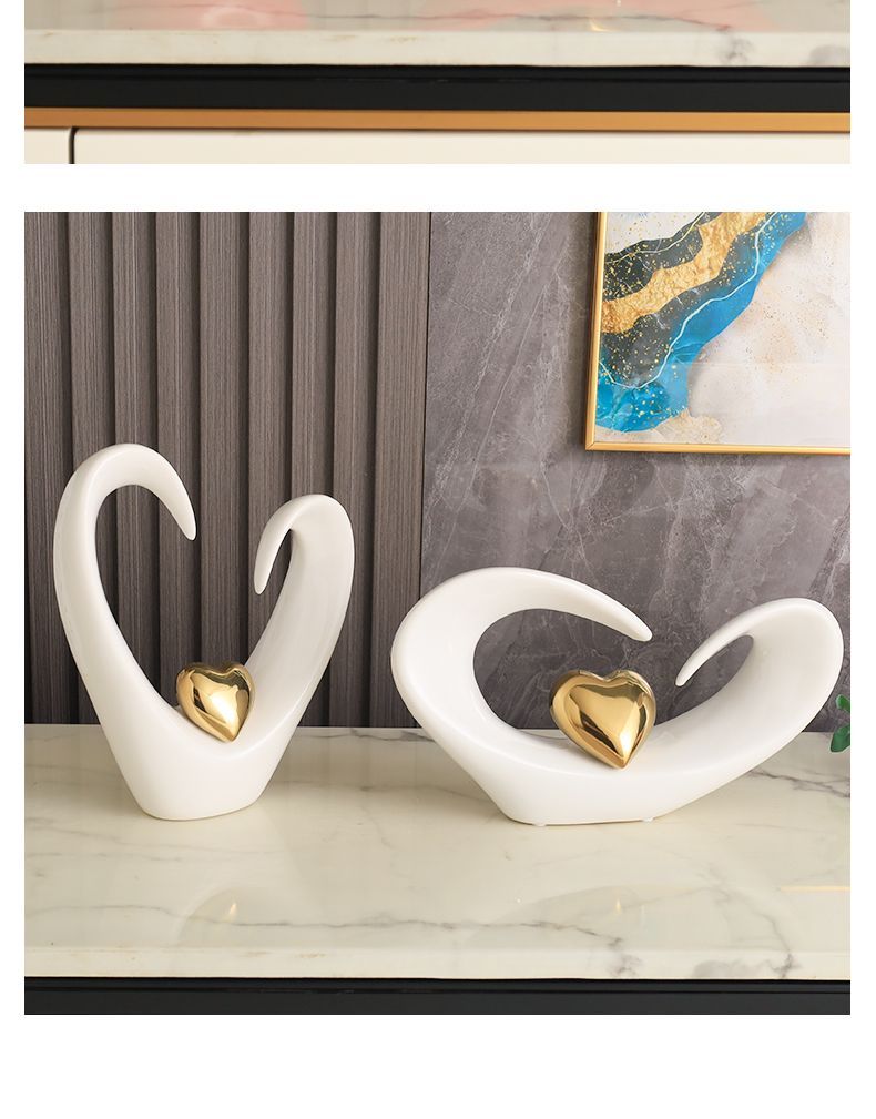 Two white abstract swan sculptures with gold centers on a marble shelf against a gray curtain backdrop.