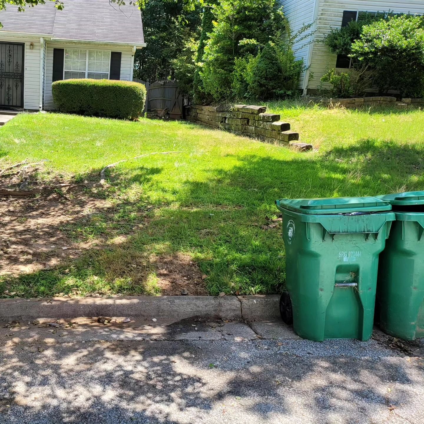 Green trash bins in front of a house with a grassy yard.