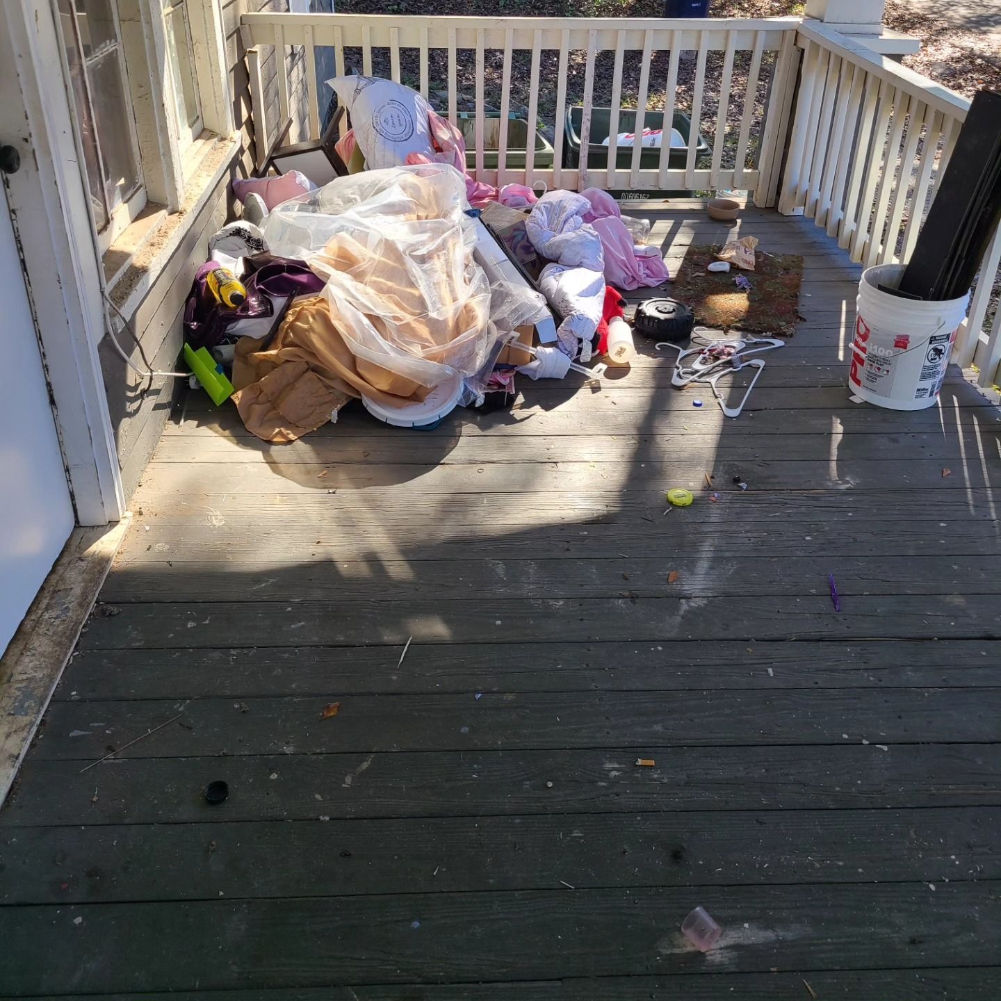 Porch cluttered with clothes, toys, and debris; white railing and trim.