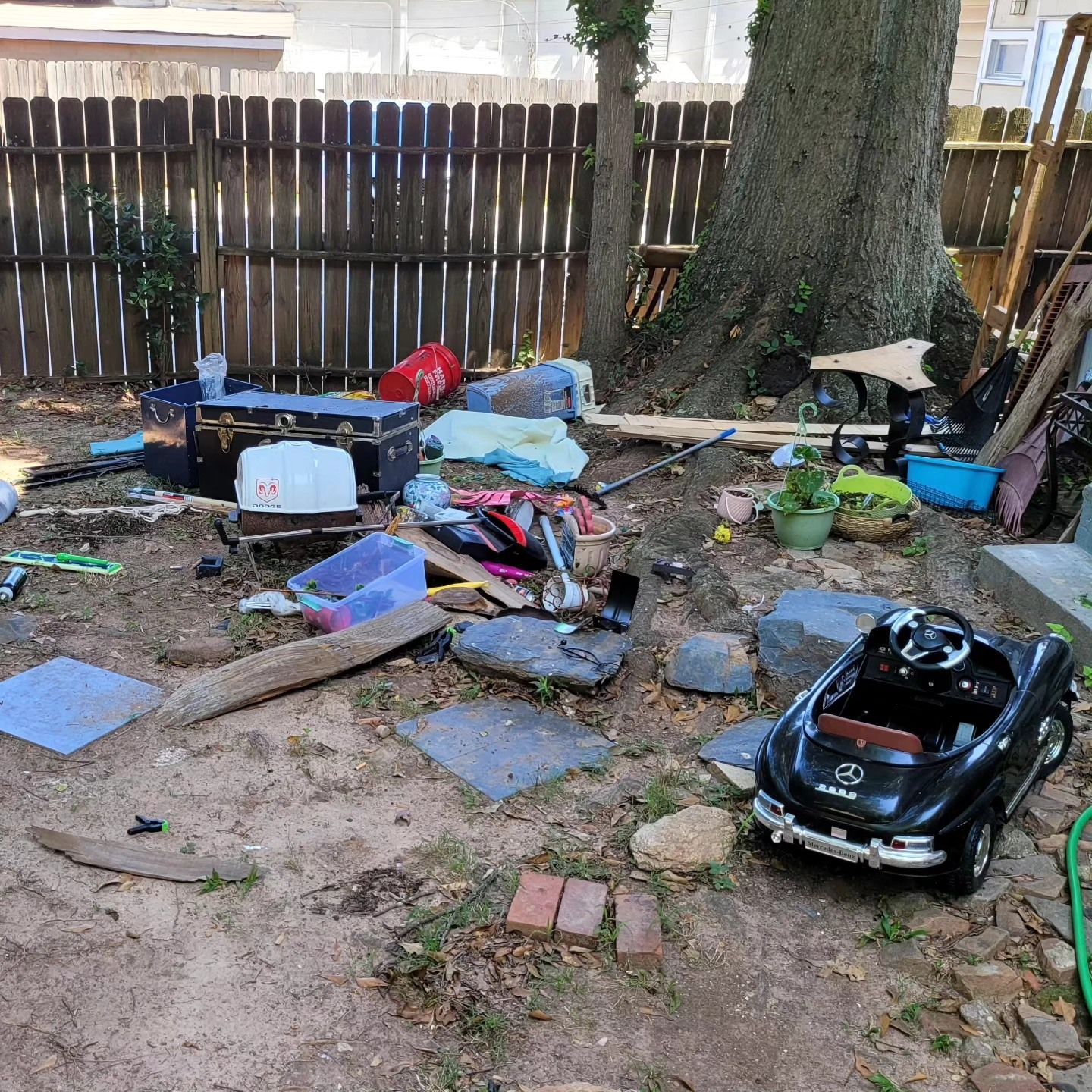 A cluttered backyard with a wooden fence, tree, toy car, and various debris.