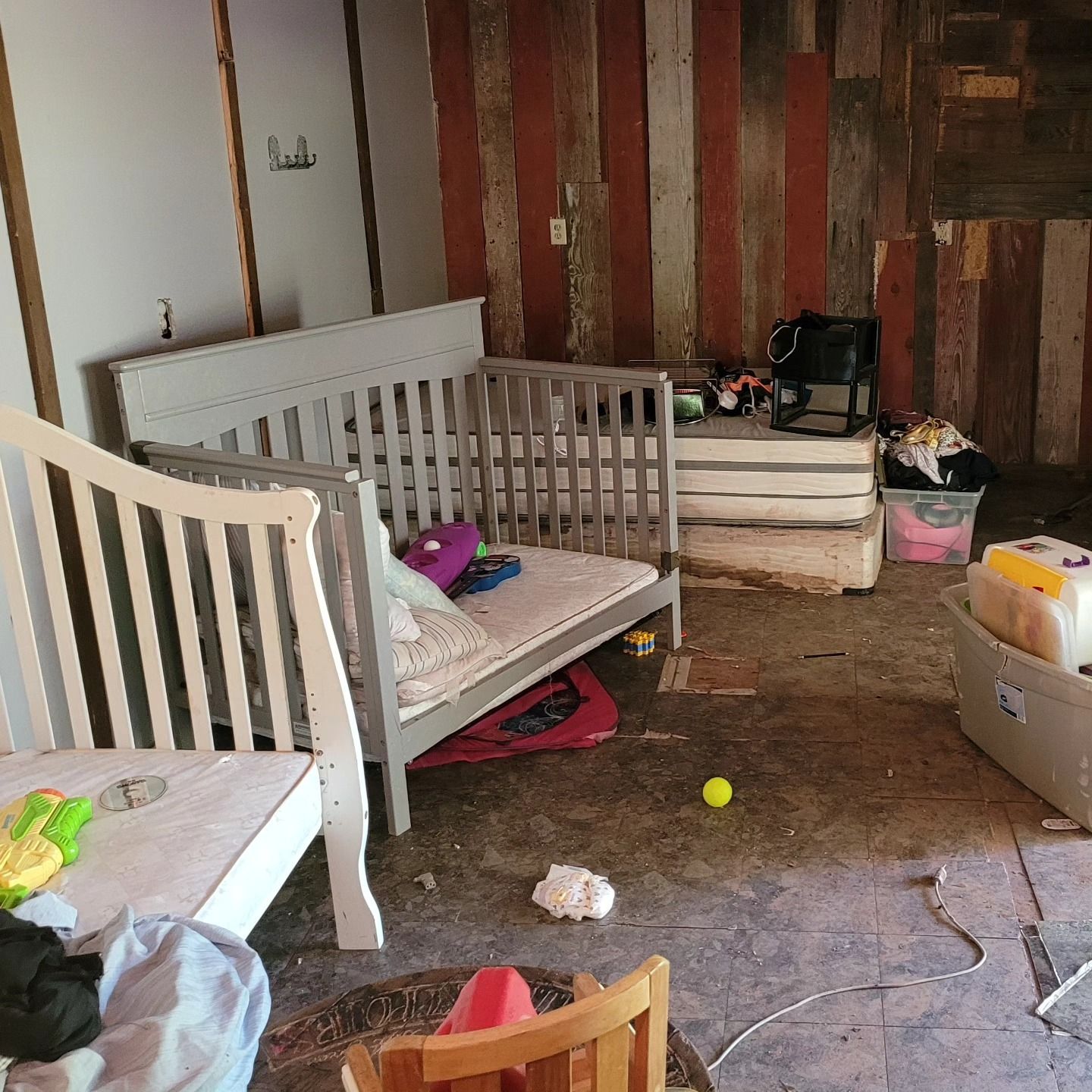 A messy room with a crib, mattress, and various items scattered on the floor and against the walls.