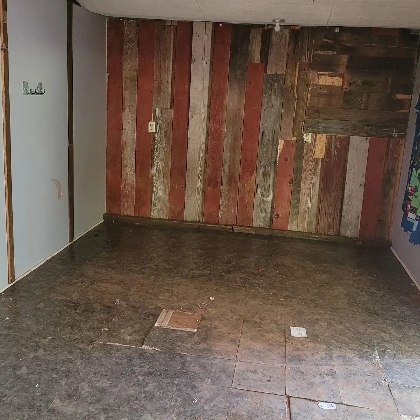 Empty room with rustic wooden wall, red and gray planks, and a concrete floor.