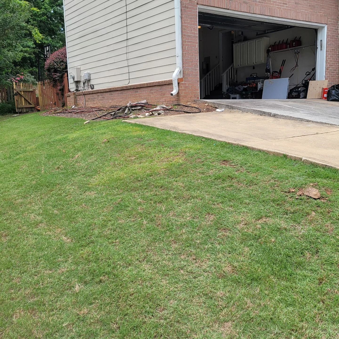Green lawn next to a concrete driveway leading to a garage. A house is in the background.