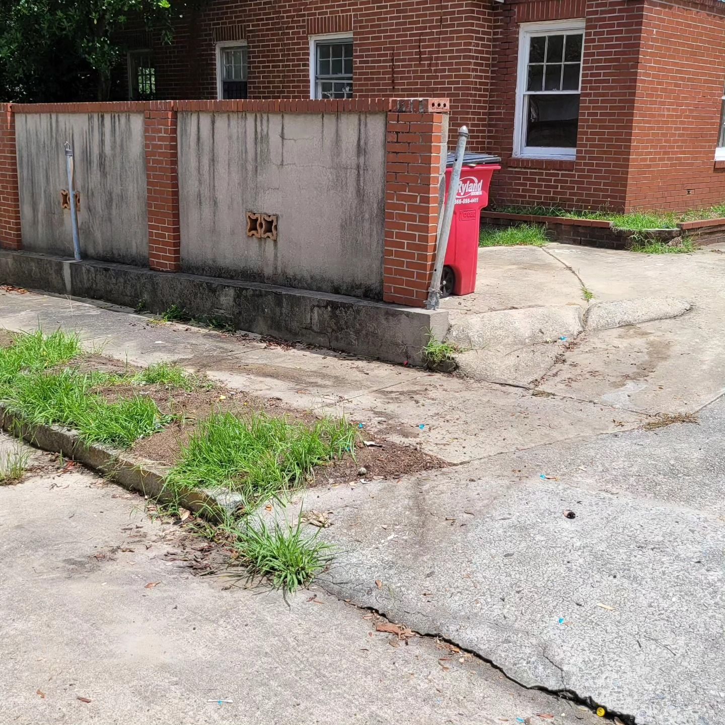 Brick building with concrete wall and cracked pavement; red trash can visible.