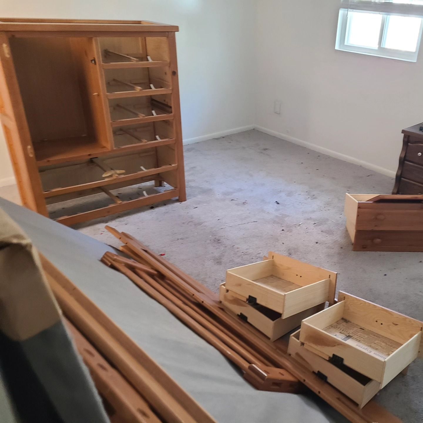 Empty wooden dresser and parts in a room with a window, cluttered carpet.