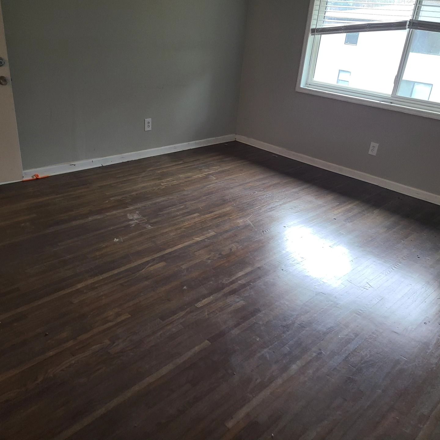 Empty room with hardwood floors, a window, and gray walls.