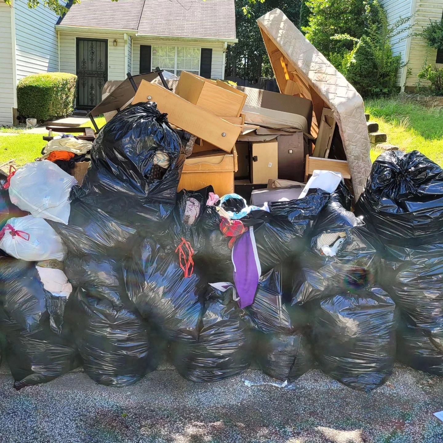 Pile of trash bags, cardboard boxes, and debris piled on a curb in front of a house.