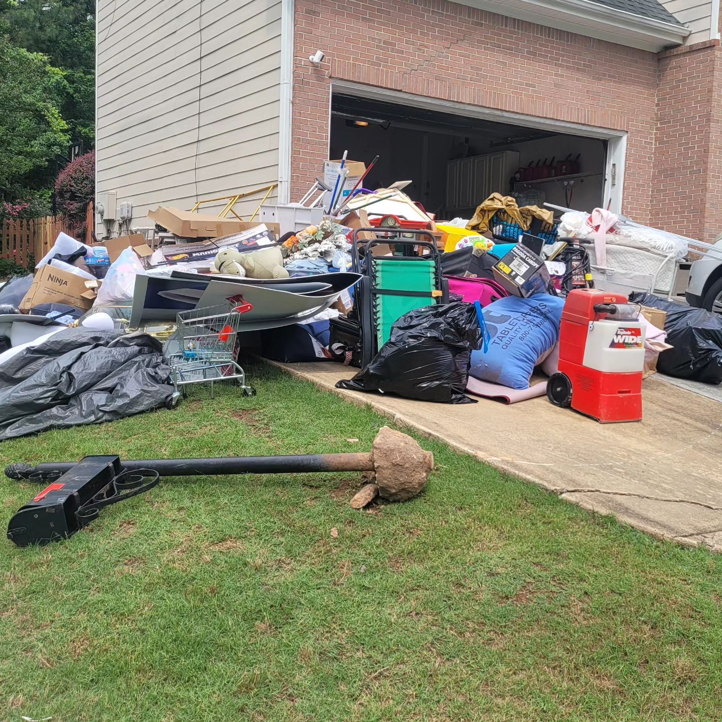 A large pile of discarded items in front of a house garage, including boxes, bags, and an electric scooter.