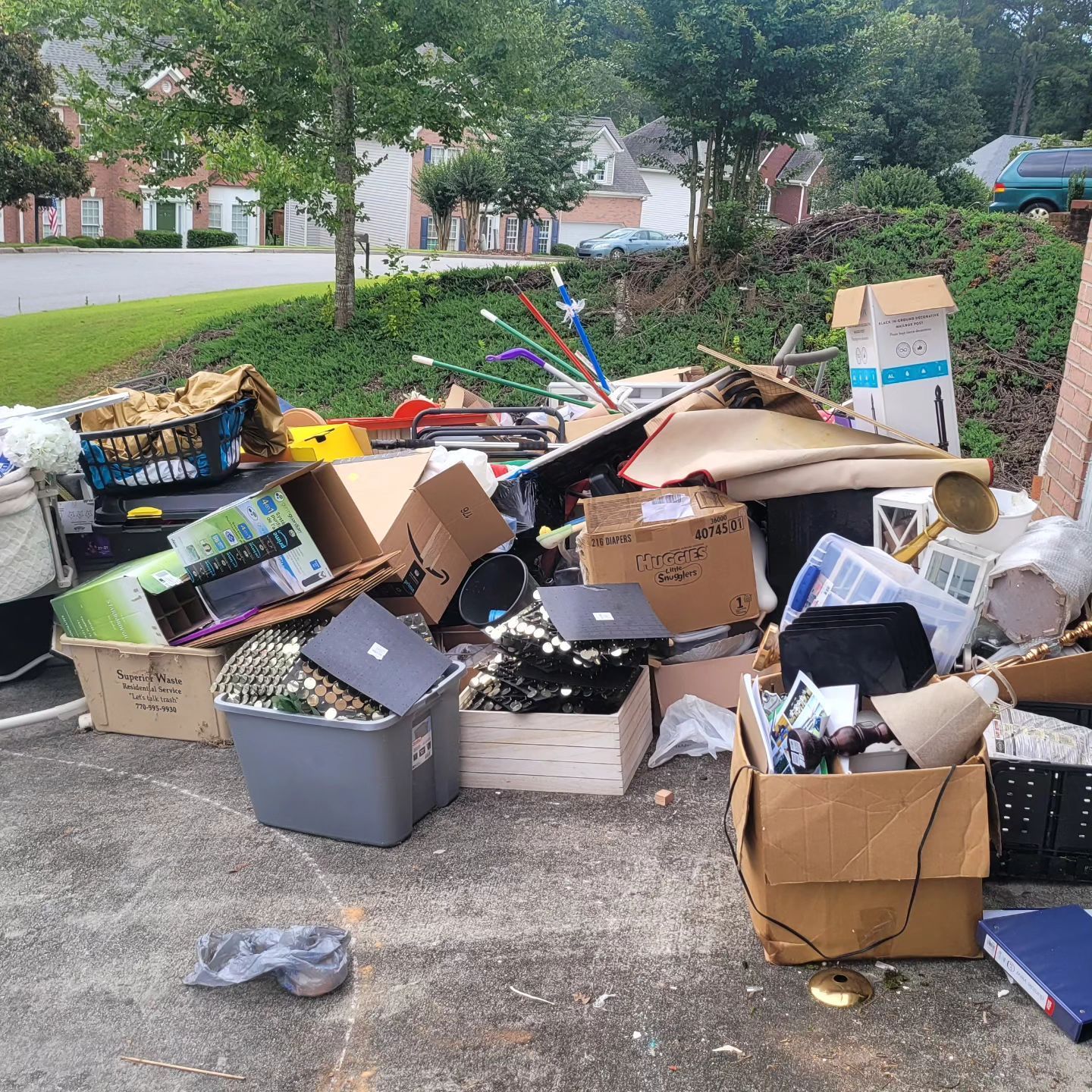 Pile of discarded items, including boxes, electronics, and debris, on a paved surface outdoors.