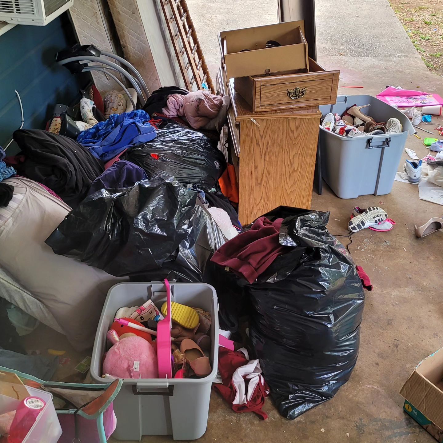 Messy garage: Black trash bags, storage bins overflowing with items, and wooden cabinet.