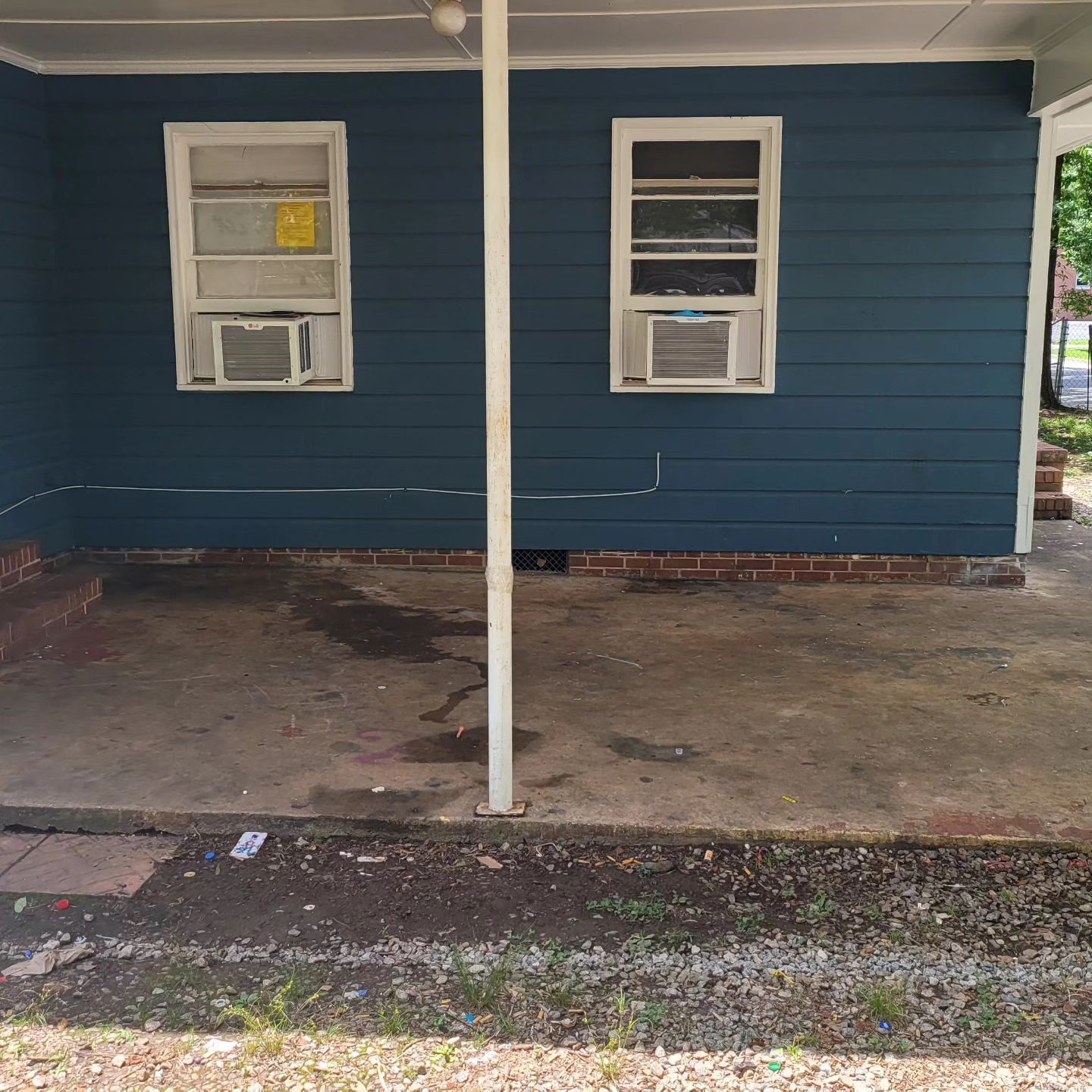 Blue-sided building with two windows each with an air conditioner. A concrete patio and grass in front.