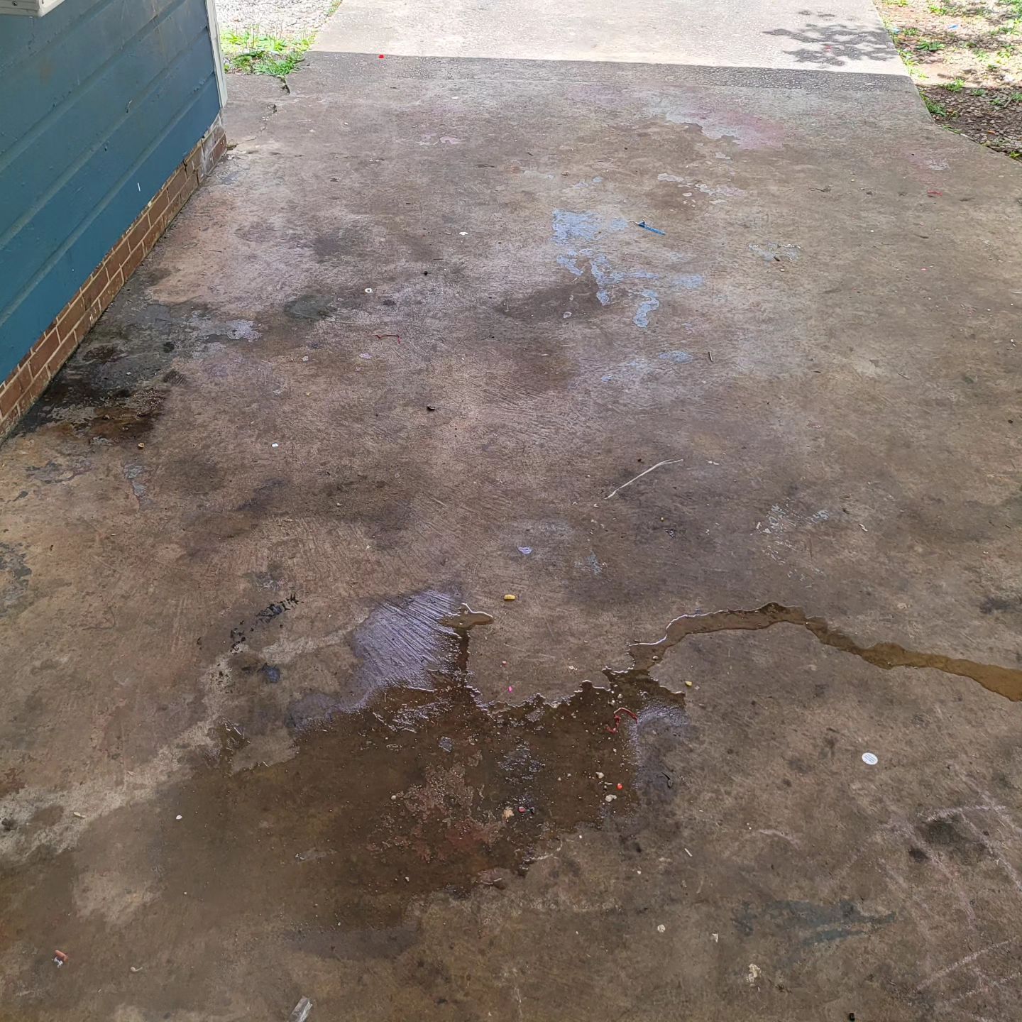 Dirty, stained concrete patio with pooled water near a blue building and a walkway.