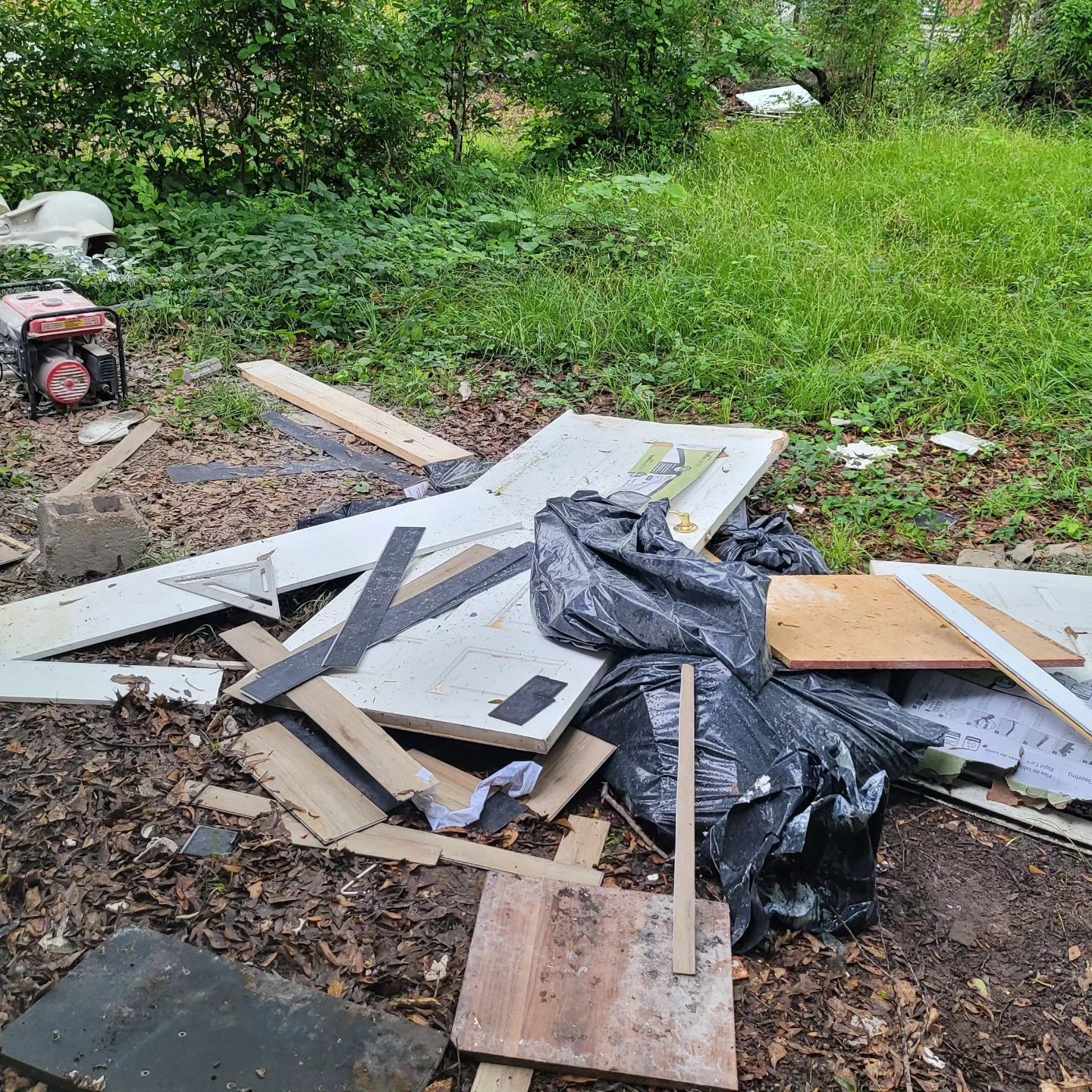 Pile of construction debris and trash in a grassy outdoor area.
