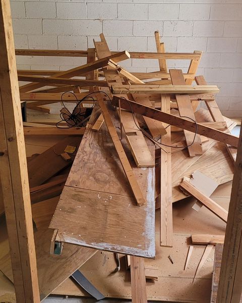 Pile of wooden debris, including boards and plywood, in a white-walled room.