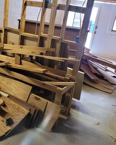 Pile of wood scraps and disassembled wooden structures in a bright room.