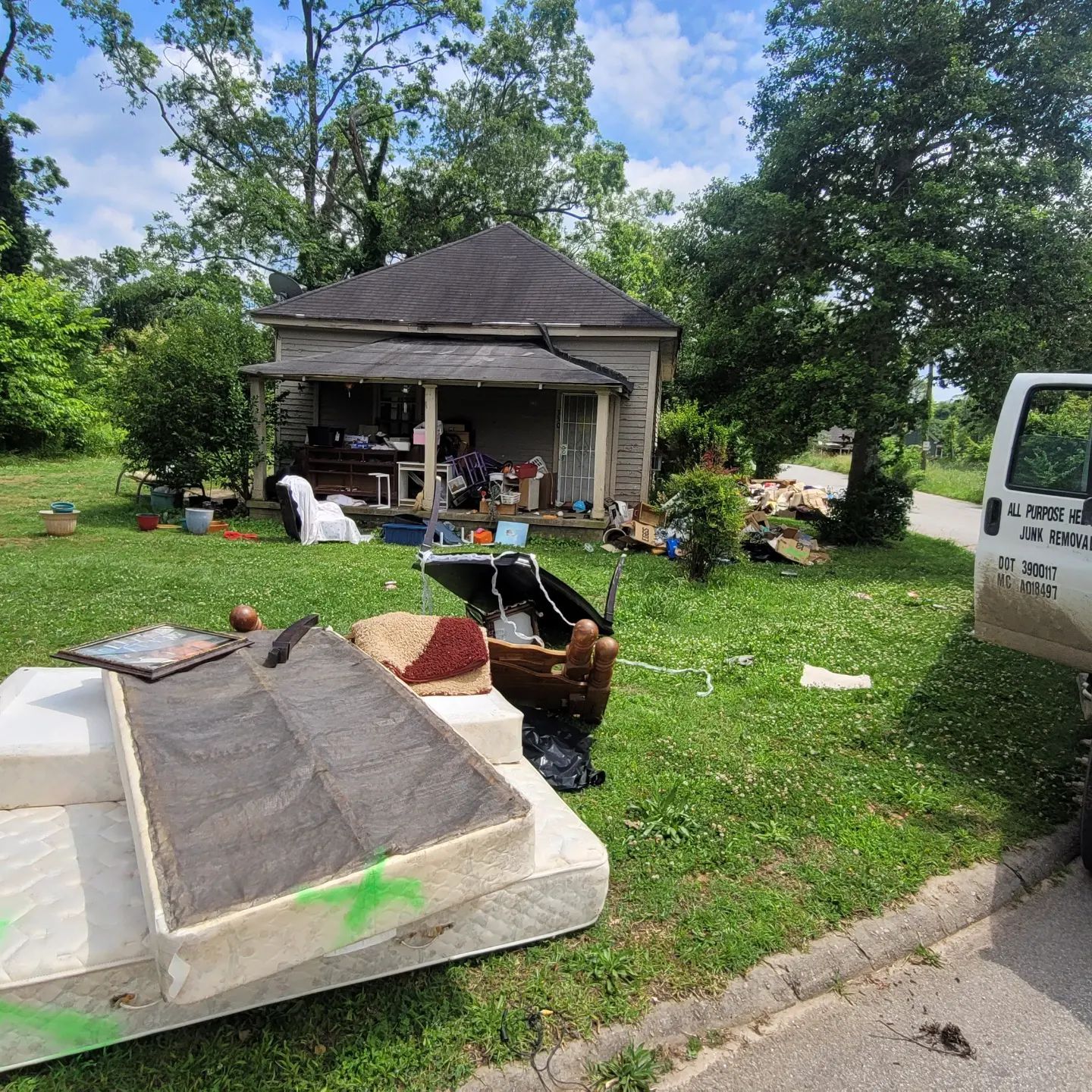 House with a cluttered porch and yard, filled with furniture and debris. White van parked nearby.