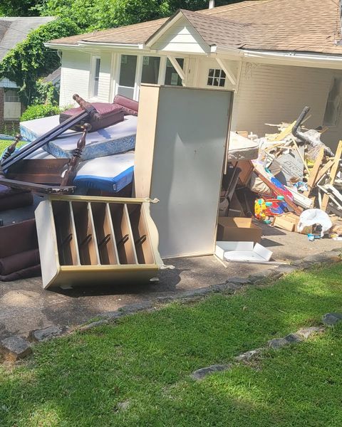 Pile of discarded furniture and debris in front of a house, including mattresses and a cabinet.