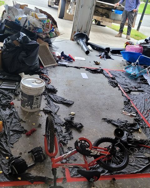 Overturned garbage with trash and bicycle on a concrete surface, near a truck, and a person.