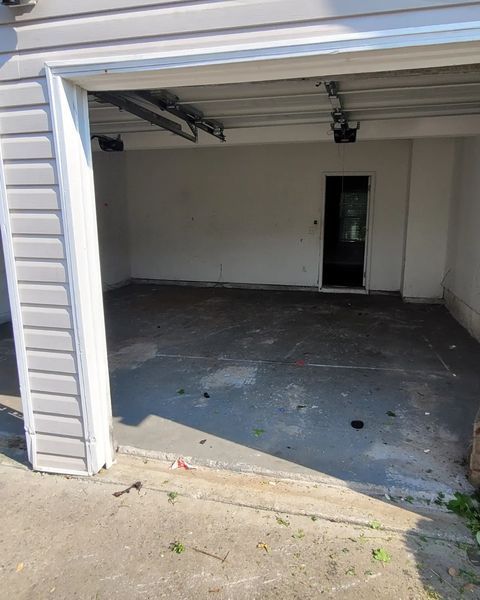 Empty garage with concrete floor, open door. Gray siding on the left.