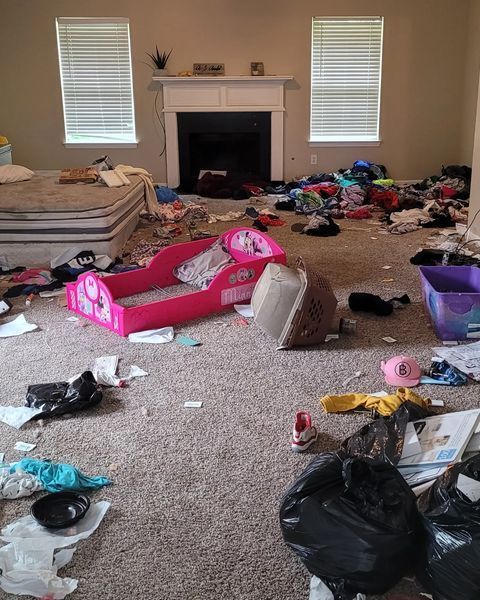 A messy living room with scattered items, children's bed, and fireplace.