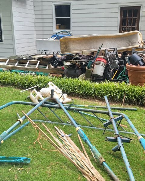 Yard with assorted debris, including a swing set, ladder, and bathtub, next to a white house.