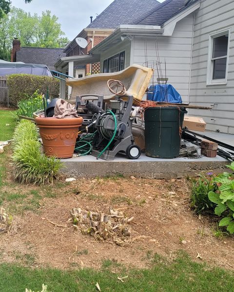Backyard cluttered with debris, including a tub, machinery, a trash can, and a large planter.