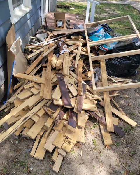 Pile of discarded wood, including planks, frames, and debris, next to a building.