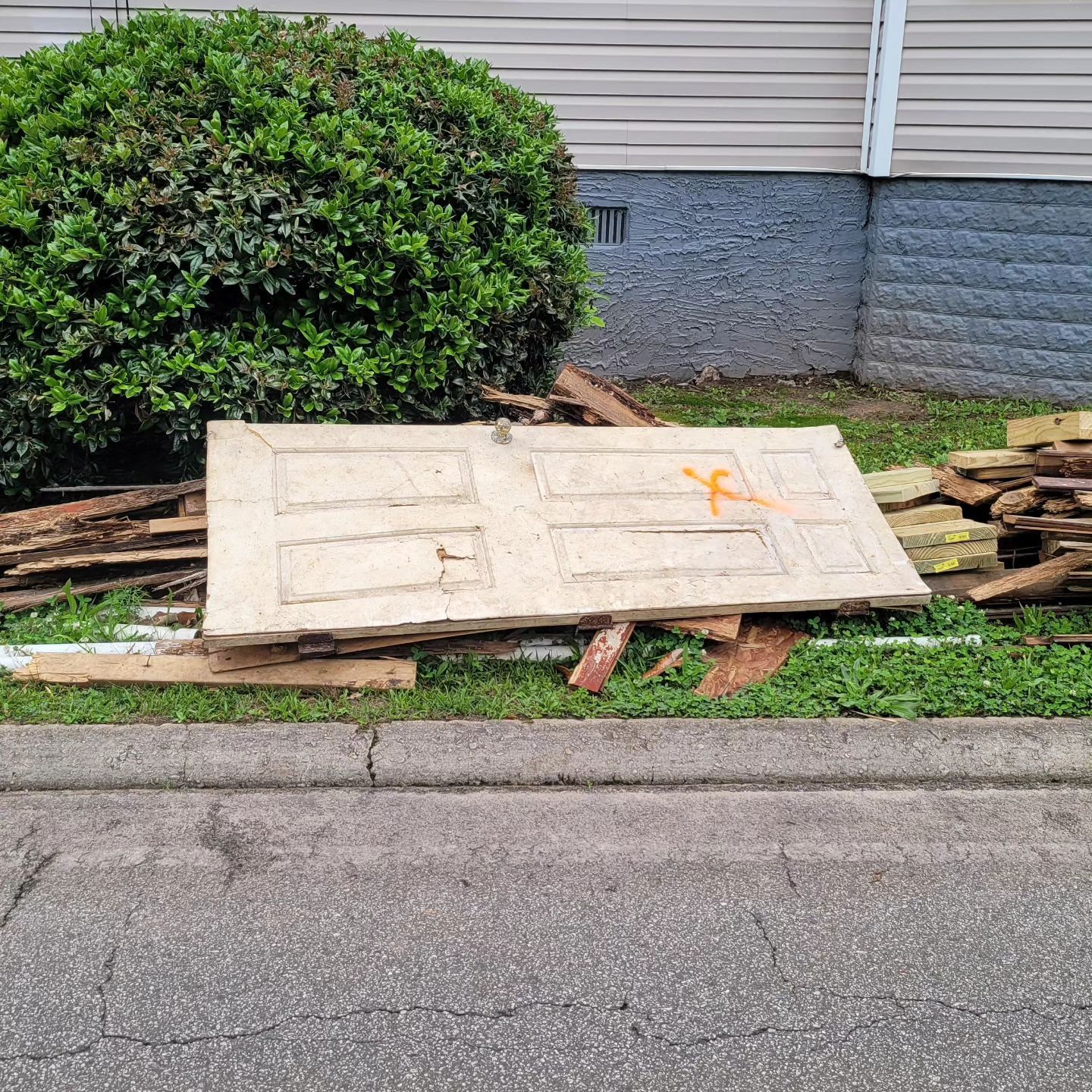 Old door and debris near a bush and building, orange marking visible.