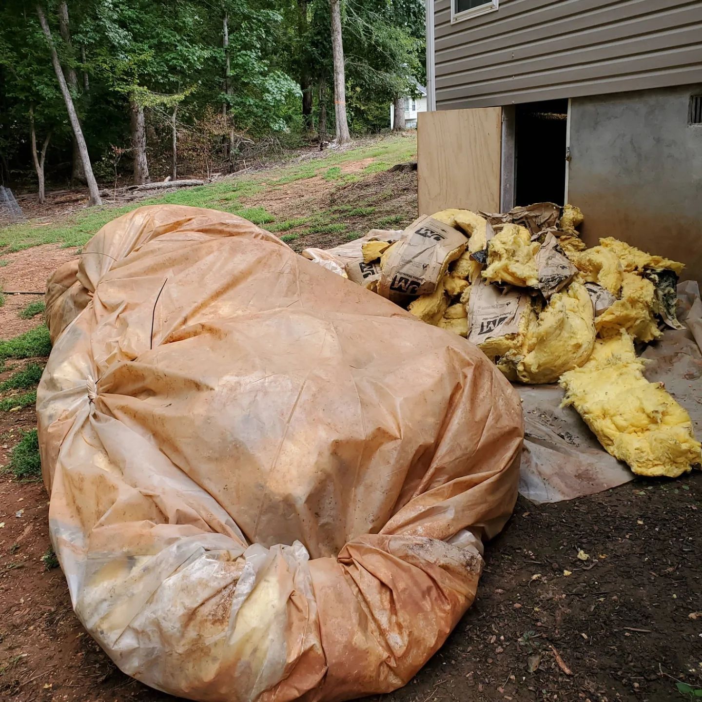 Large brown bag and pile of yellow insulation next to a house with an open door.