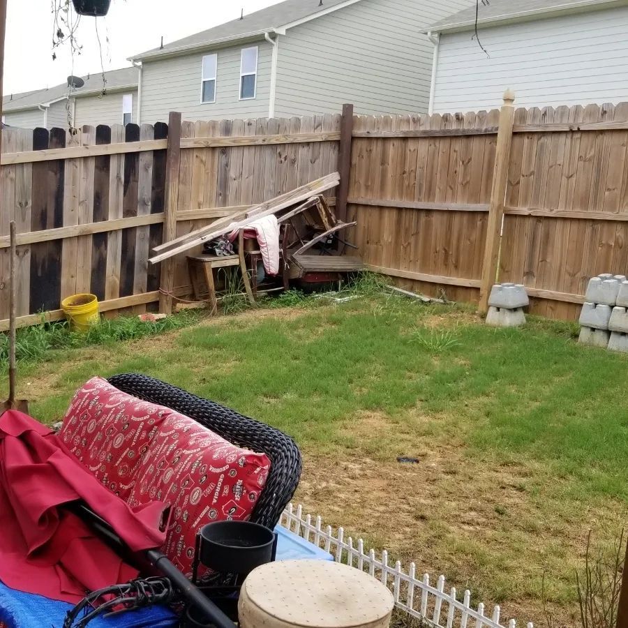 A cluttered backyard with a wooden fence, grass, and miscellaneous items.
