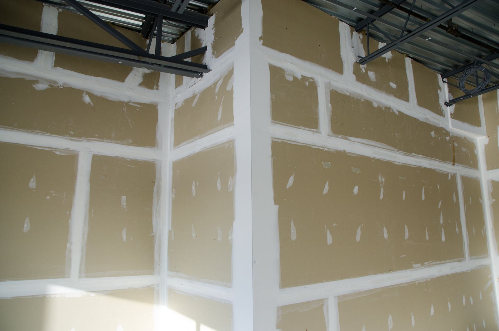 Drywall installation in progress; beige walls with white joint compound filling seams and corners.