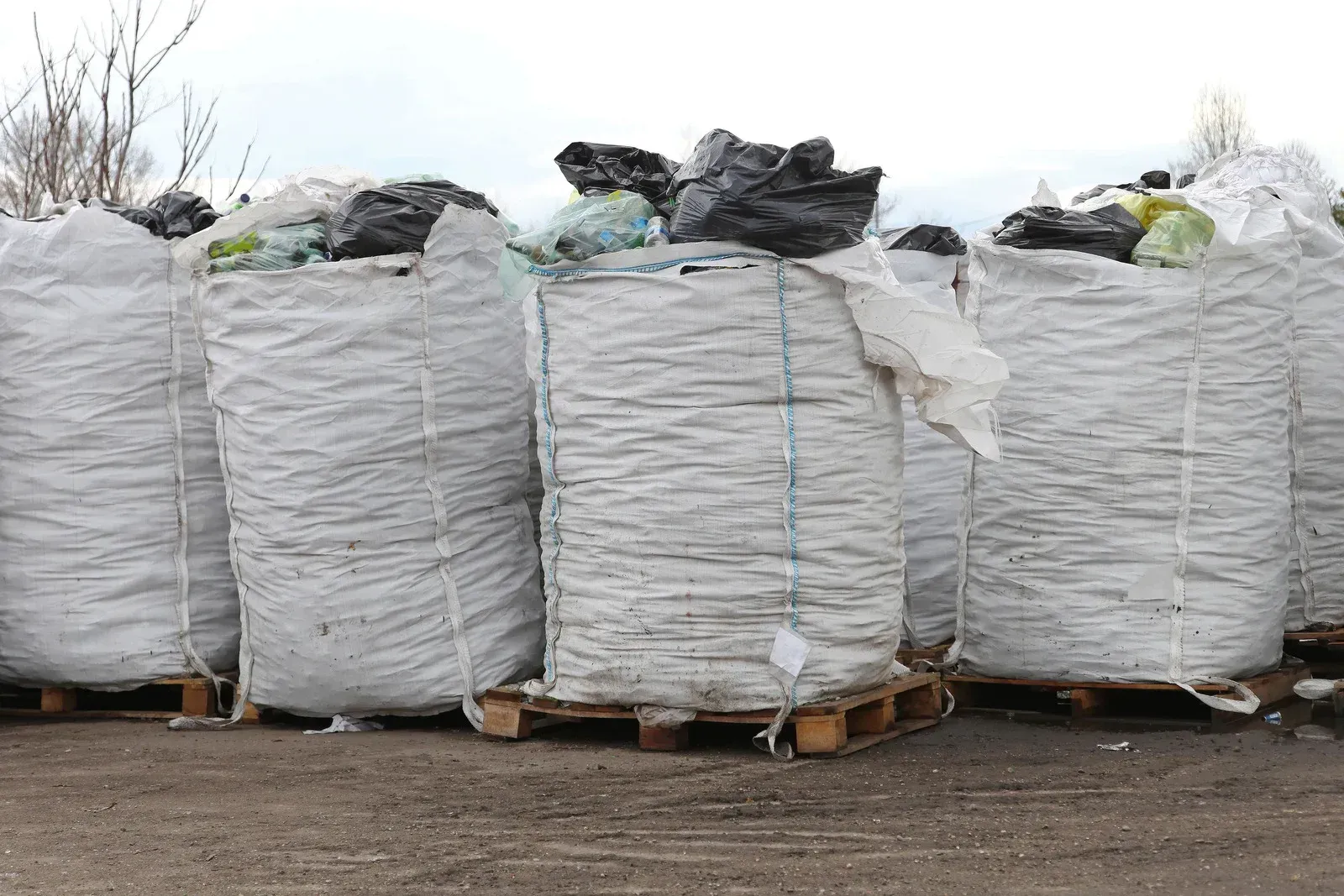 Large white bags filled with what appears to be recycled materials, stacked on wooden pallets outdoors.