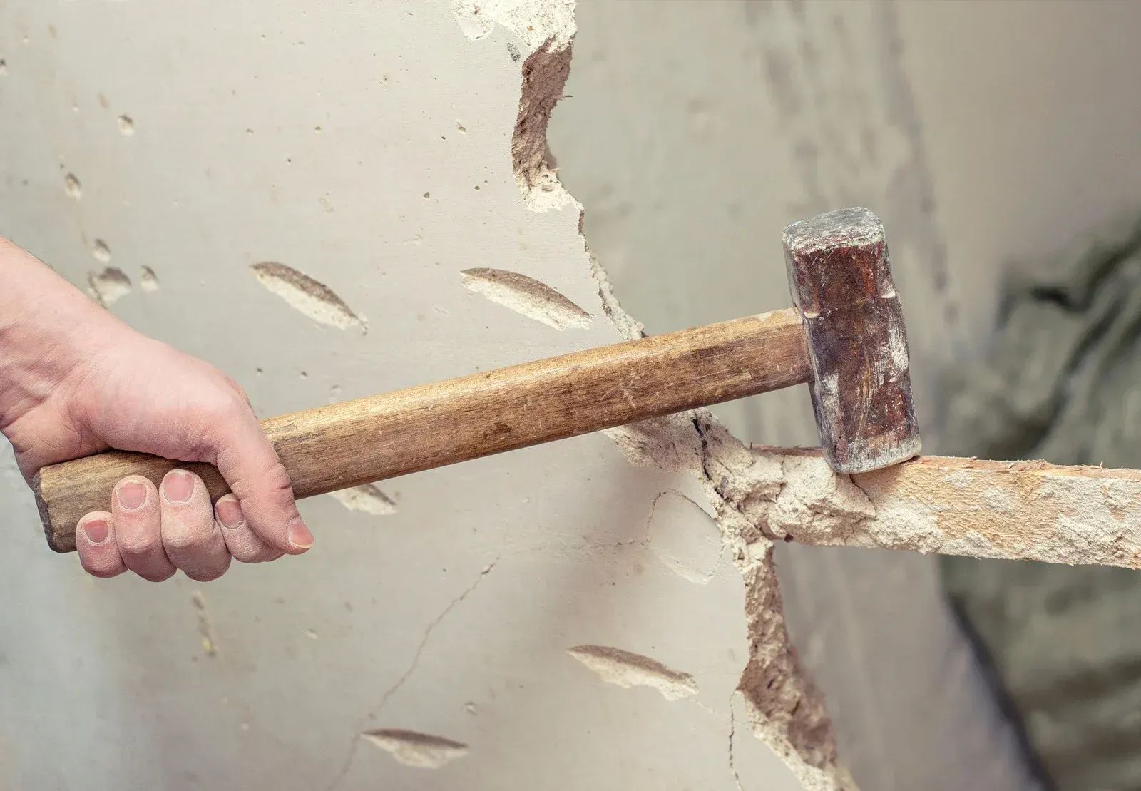 Hand using a hammer to break a hole in a wall.