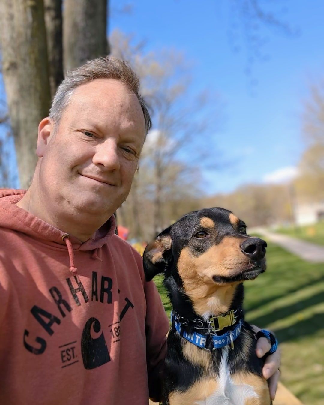 A dog trainer poses outdoors with his black and tan dog on a sunny day. Dog trainer in Birmingham MI. 